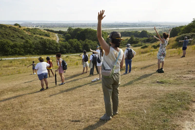 A group of people with arms in the air on a hill facing the Estuary wearing headphones